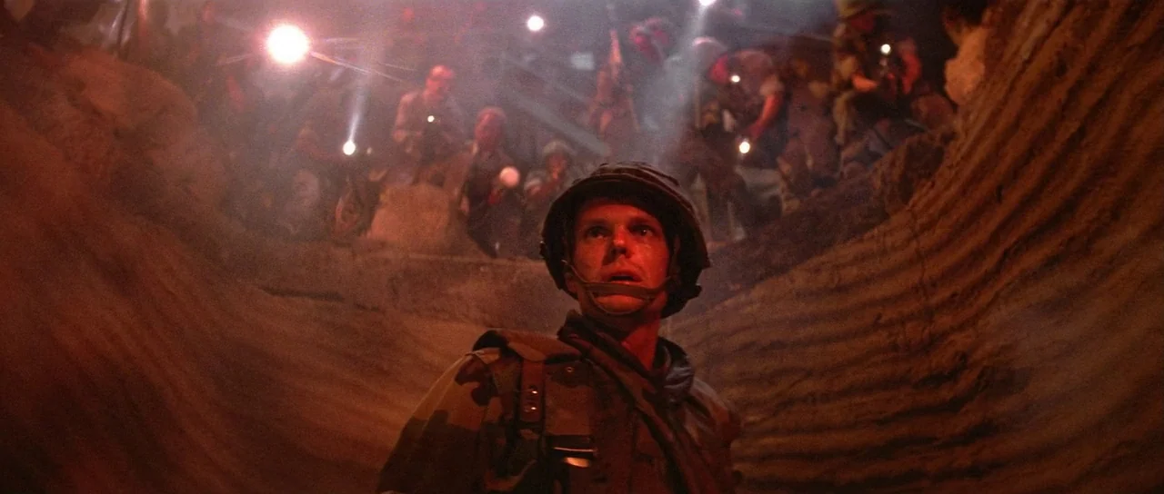 Invaders From Mars (1986) movie still: medium — A deep earthen trench filled with thick atmosphere and haze at night. A lone soldier stands in the…