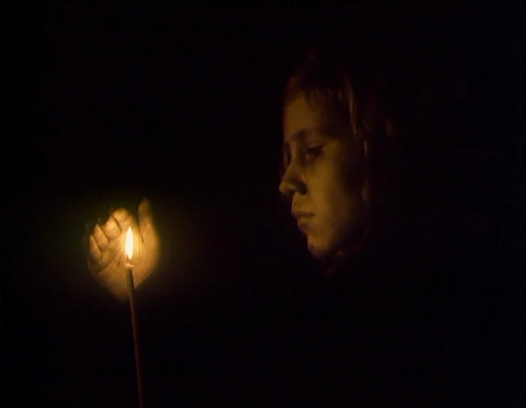 Dead Man’s Letters (1986) movie still: closeup — A person stands in total darkness illuminated only by the light of a candle. The warm flame casts…