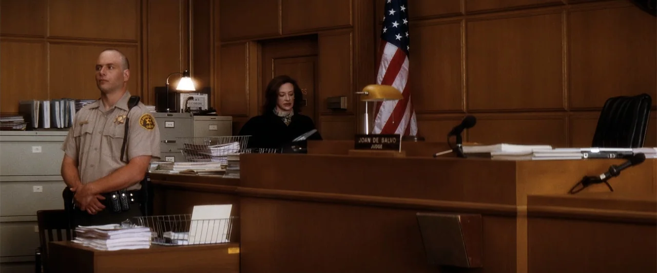My Sister's Keeper (2023) movie still: medium — A wood-paneled judicial bench stands in front of a wall with an American flag. A law enforcement…