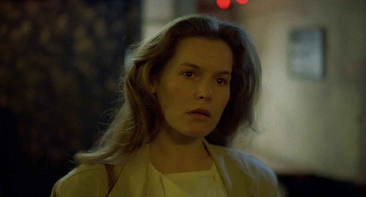 Barfly (1987) movie still: closeup — A dimly lit indoor space with soft greenish ambient light casting long shadows. A woman stands in the…