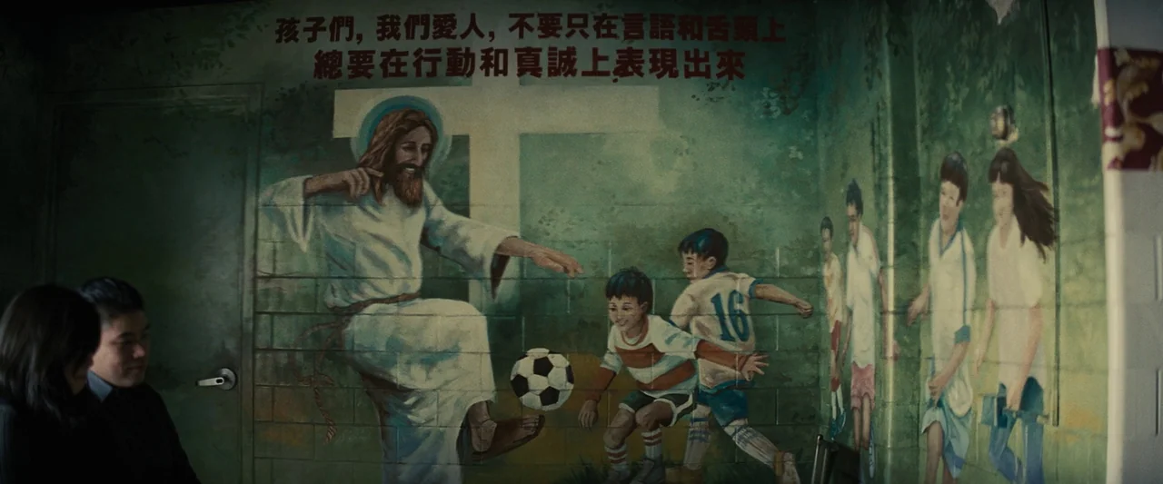 Knock at the Cabin (2023) movie still: medium — An interior space features a large mural depicting Jesus playing soccer with local children. Two…