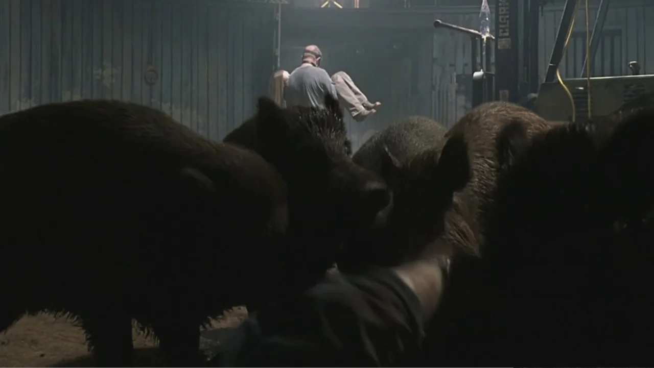 Hannibal (2001) movie still: wide — A dark, smoky interior of an industrial building with corrugated metal walls and dirt floor. A man walks away…