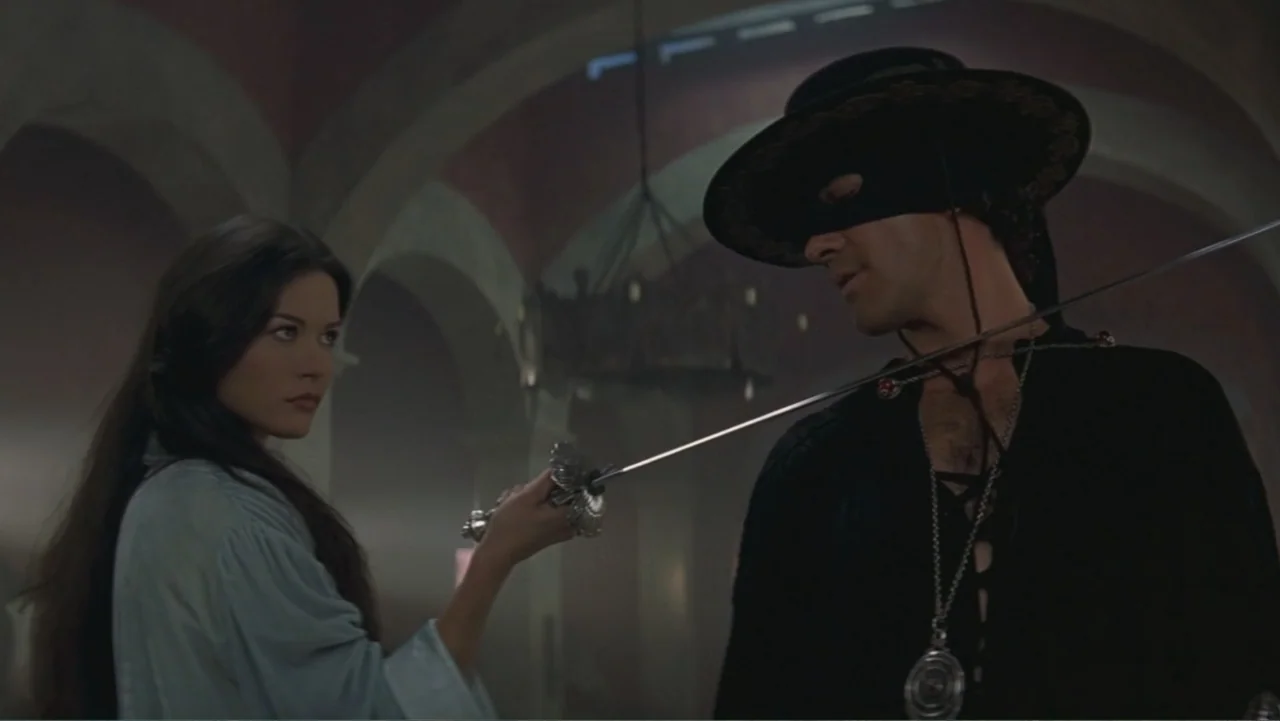 The Mask of Zorro (1998) movie still: medium — A stone hallway with arched ceilings and a large iron chandelier overhead. A woman points a sword at…