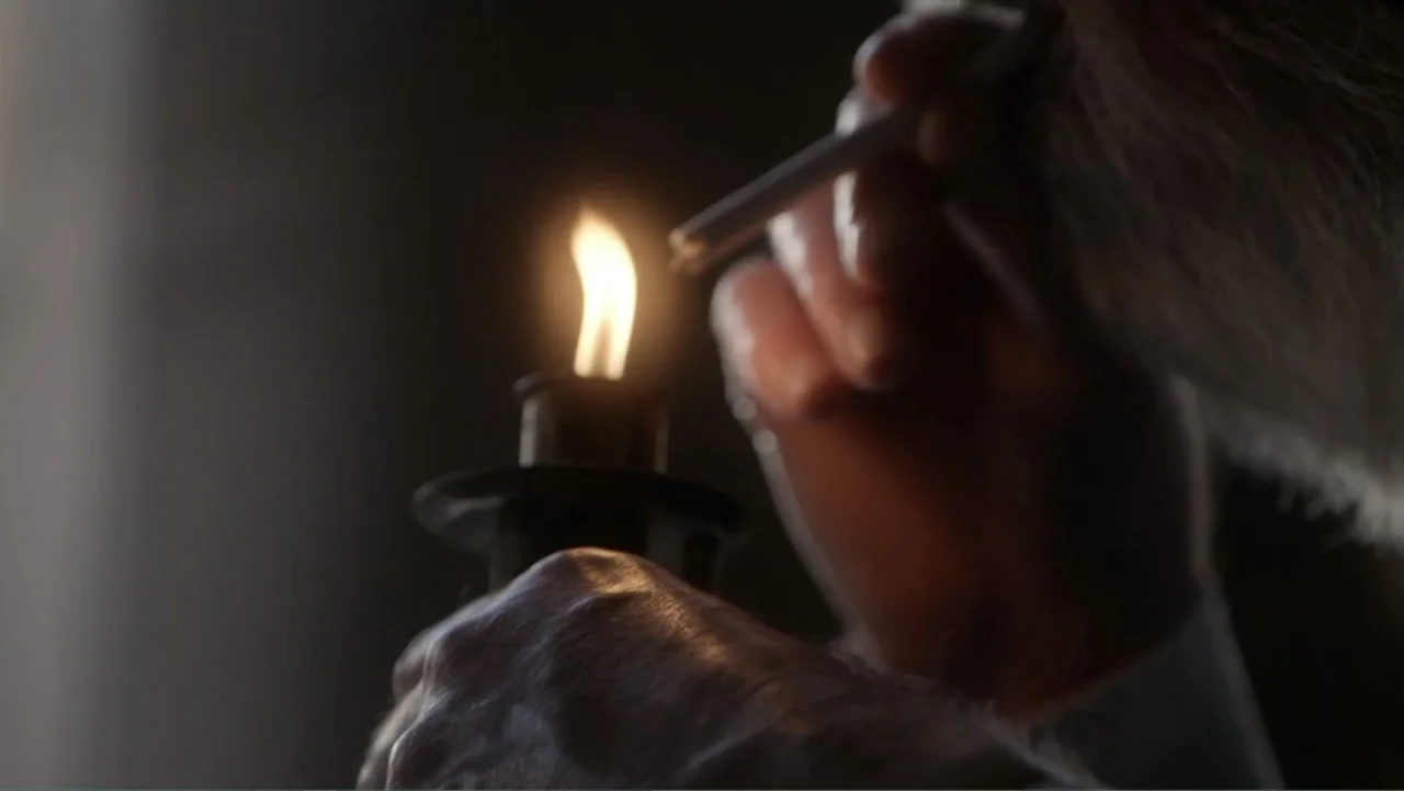 Almost Human: Rise of the Apes (2022) movie still: closeup — A dark indoor space is dimly lit by a single small flame. A hand holds a cigarette near…