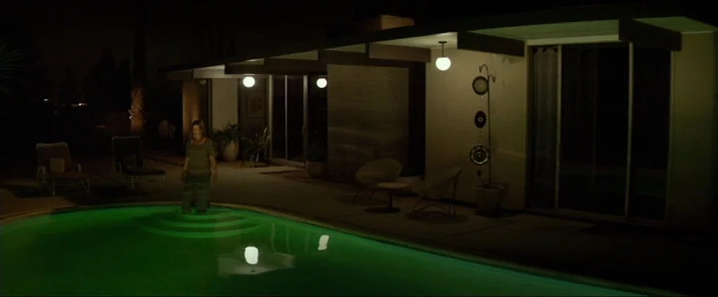 Cake (2014) movie still: wide — A modern mid-century home exterior features a wide patio next to a swimming pool. A woman stands in the shallow end…