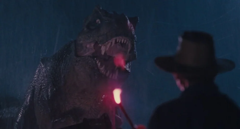Jurassic Park (1993) movie still: medium — A dark, rainy outdoor environment at night with heavy precipitation visible in the air. A man in a hat…