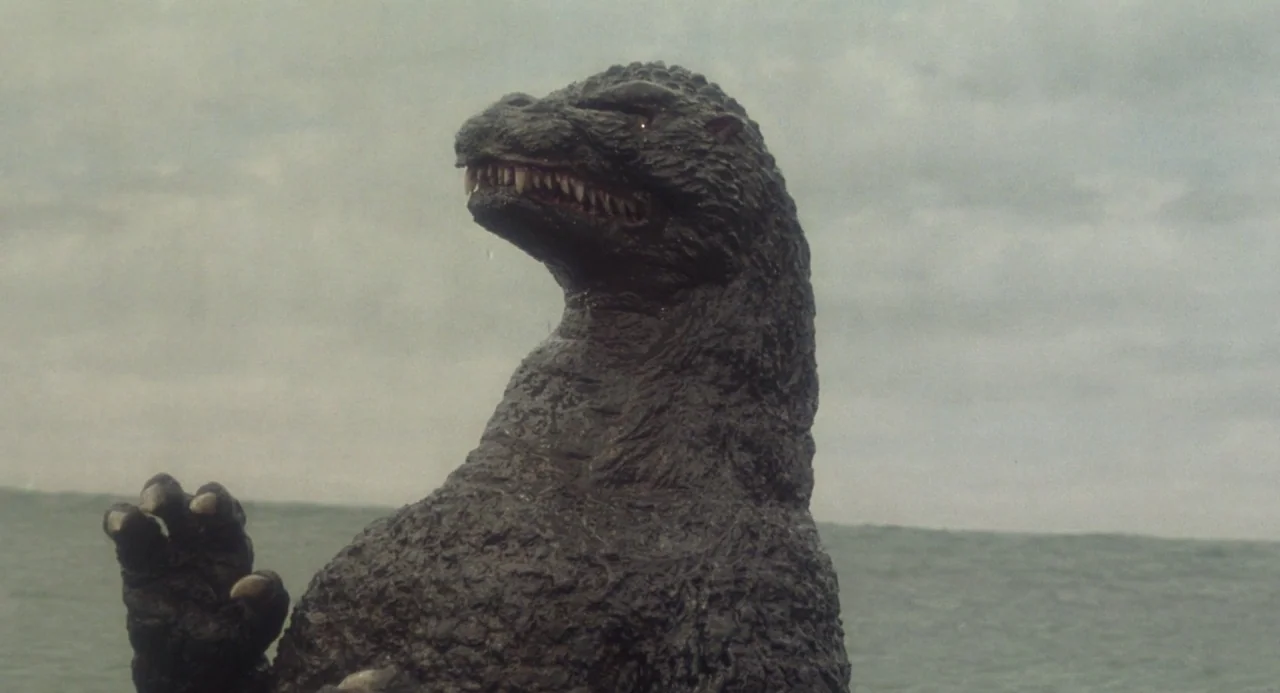 Godzilla vs. King Ghidorah (1991) movie still: medium — A dark, textured reptilian creature surfaces in an expansive, grey ocean under overcast…