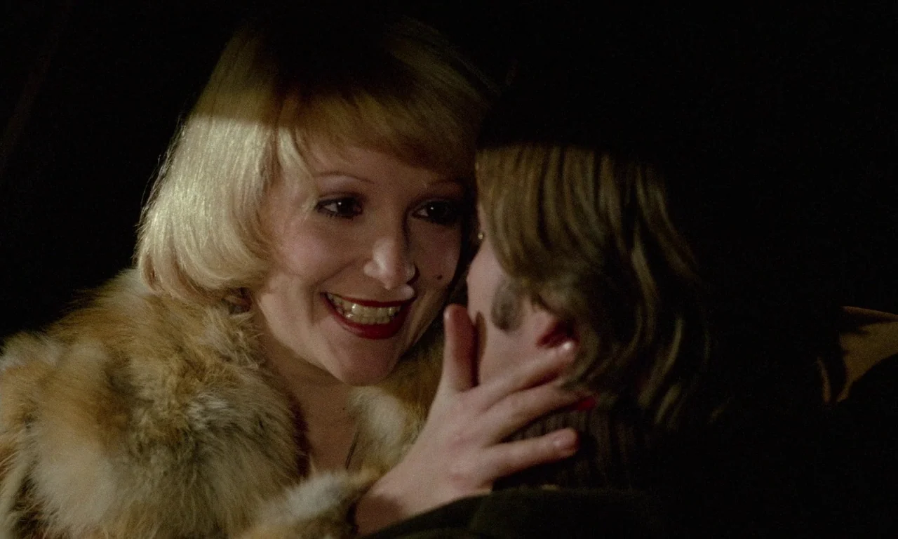 The Margin (1976) movie still: closeup — The interior of a vehicle at night with a dark background. A woman wearing a fur collar reaches out to…
