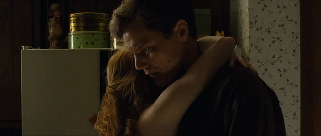 Take Shelter (2011) movie still: medium — A residential setting with floral patterned wallpaper and a white refrigerator in the background. A man…
