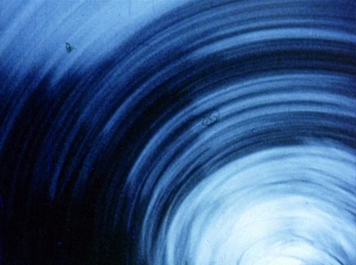 Slacker (1991) movie still: establishing — An abstract field of swirling blue lines radiates from a bright central point. Visible film grain and…