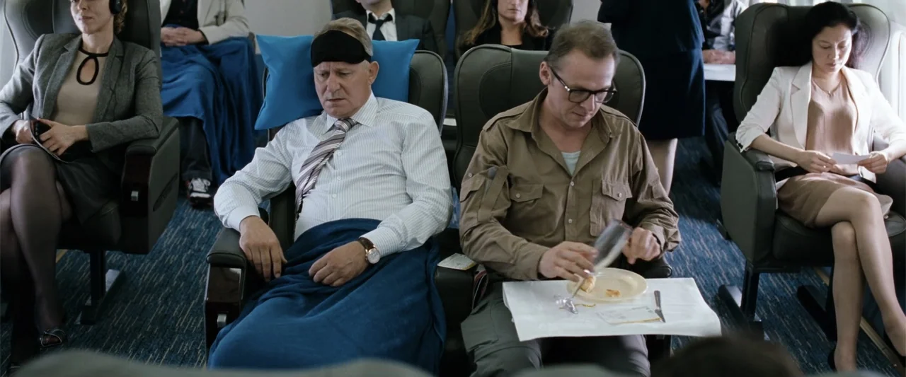 Hector and the Search for Happiness (2014) movie still: medium — The interior of a commercial airplane cabin shows two men sitting in adjacent…