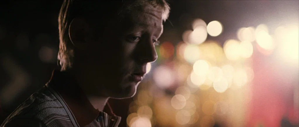 The Scouting Book for Boys (2009) movie still: closeup — A man stands in an outdoor area at night with blurred decorative lights. He looks downward…