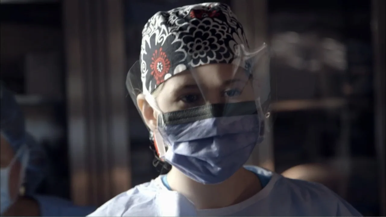 Aliens Inside Us (2013) movie still: closeup — A medical professional wears surgical scrubs and a clear protective face shield. She stands in a…