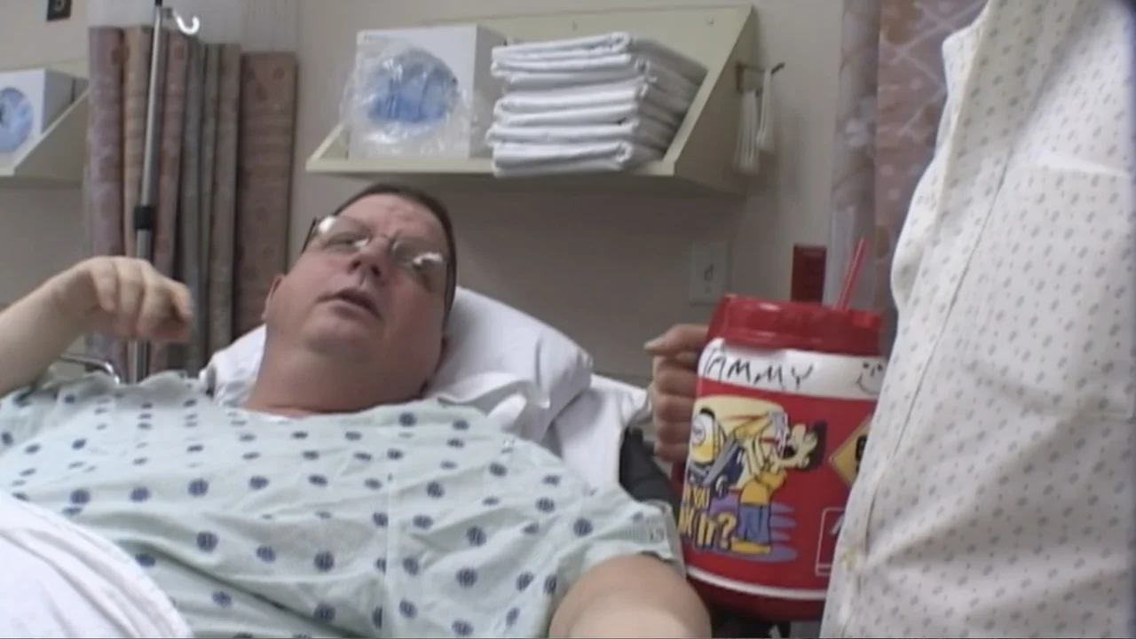 Super Size Me (2004) movie still: medium — A hospital room features medical supplies stacked on shelves and a curtained background. A patient in a…