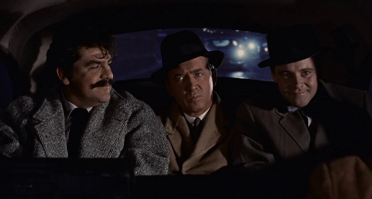 Bell Book and Candle (1958) movie still: medium — Three men sit side-by-side in the backseat of a dark car at night. Outside the rear window, bright…