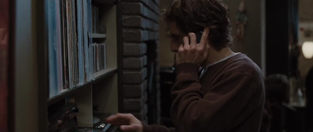 Greenberg (2010) movie still: medium — A living room interior features a brick fireplace and shelves filled with vinyl records. A young man wearing…