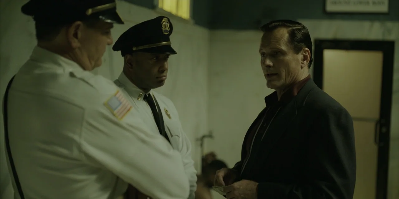 Green Book (2018) movie still: medium — A utilitarian restroom features tiled walls and a stark doorway in the background. Two police officers…