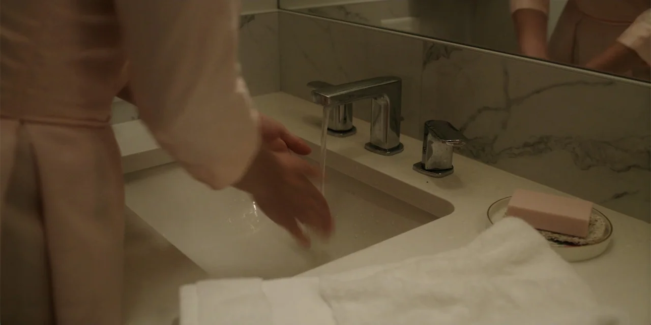 Totally Killer (2023) movie still: medium — A modern bathroom features a white marble vanity with chrome fixtures and a mirror. A person in a pink…