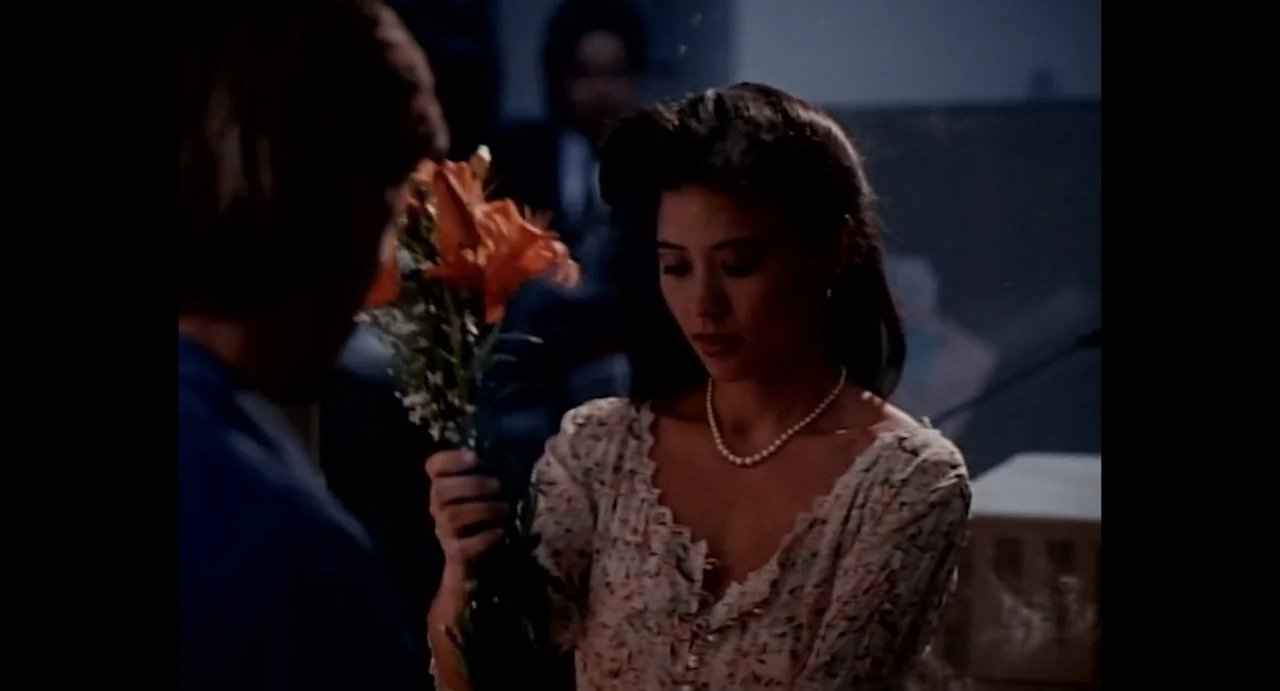 American Yakuza (1993) movie still: medium — A dimly lit room at night features a man giving flowers to a woman. The woman looks down at the orange…