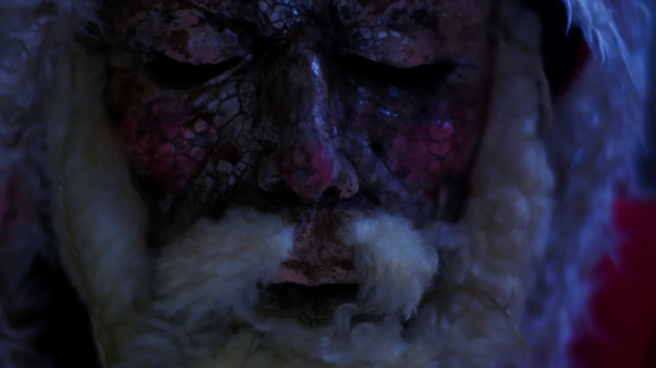 Carnage for Christmas (2024) movie still: closeup — The frame shows a close-up of a face with severely cracked, textured, dark skin. A white…