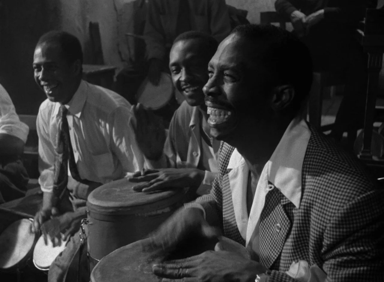 Victims of Sin (1951) movie still: medium — Three men play conga drums in a dimly lit, crowded musical space. They are laughing while performing,…