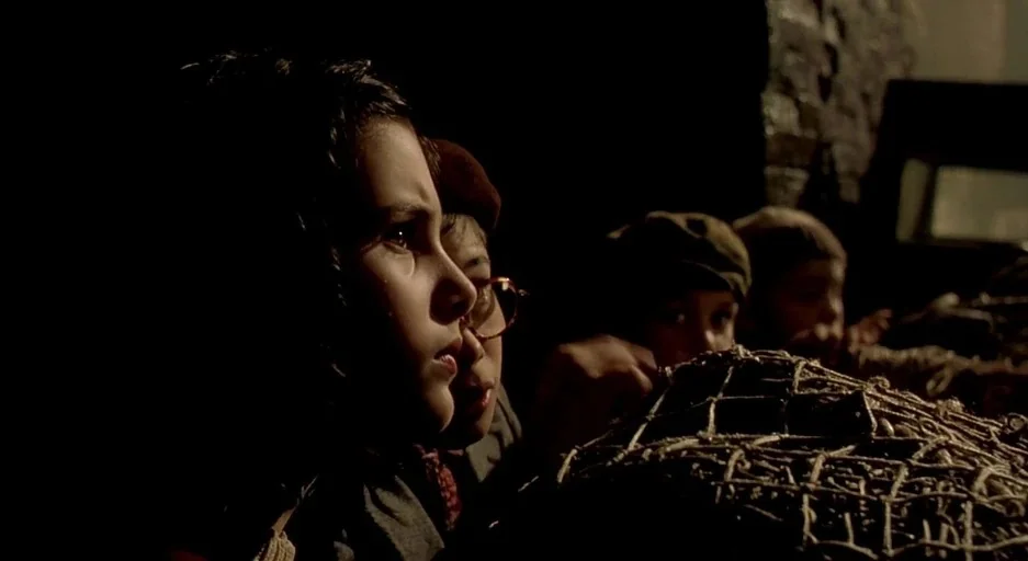 The City Of Lost Children movie still: medium — A group of children watch from a darkened, unidentifiable interior space. They gaze collectively…