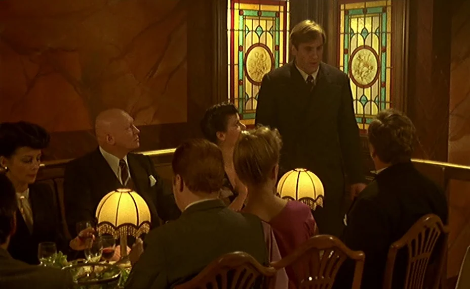 The Last Metro (1980) movie still: medium — A dimly lit, wood-paneled room features stained-glass windows and circular table lamps. A group of…