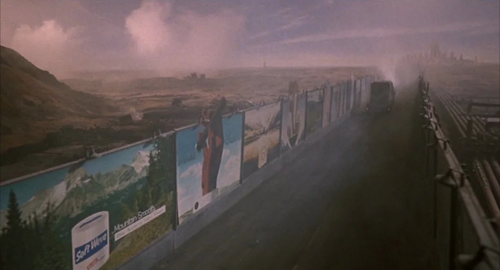 Brazil (1985) movie still: establishing — A long stretch of road features a line of billboards depicting natural landscapes. A lone vehicle travels…