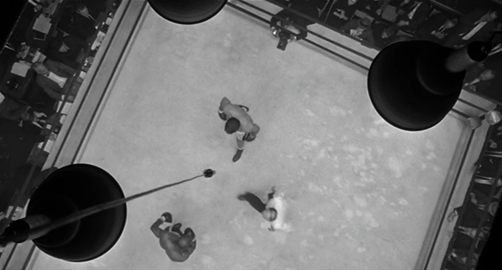 The Hurricane (1999) movie still: wide — A square canvas floor is surrounded by blurred figures sitting in dark, crowded stands. Two boxers and a…