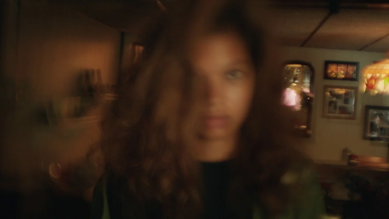 Madeline’s Madeline (2018) movie still: closeup — A domestic interior space with walls adorned by small framed pictures and mirrors. A person with…