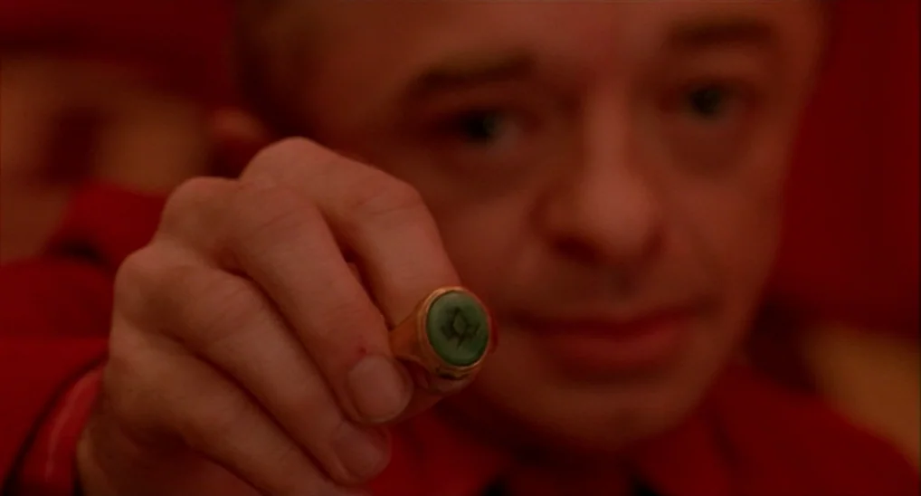 Twin Peaks: Fire Walk With Me (1992) movie still: closeup — A man stands in a dimly lit, saturated red interior space. He holds a gold ring with a…