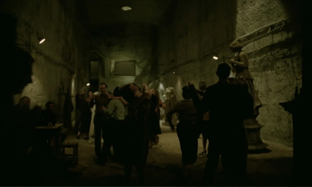 The Brutalist (2024) movie still: wide — A cavernous stone basement features rough walls and scattered industrial or antique objects. A small group…