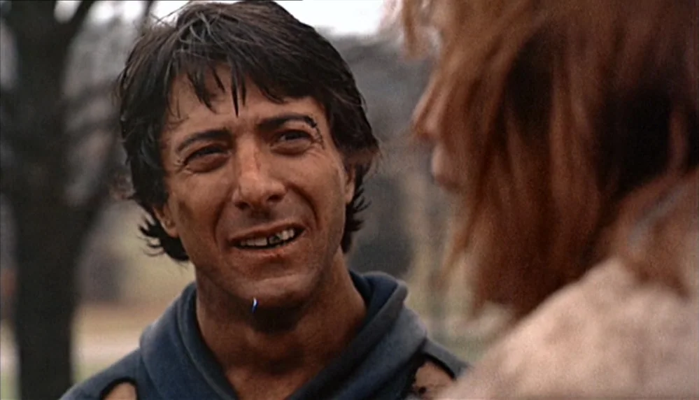 Marathon Man (1976) movie still: closeup — An outdoor area with blurred trees and foliage visible in the background. A disheveled man with dirt on…