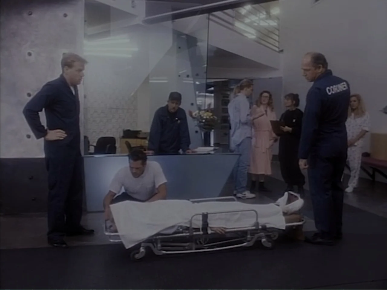 Firepower (1979) movie still: wide — A modern, spacious interior with glass partitions and metal accents houses a medical work area. A group of…