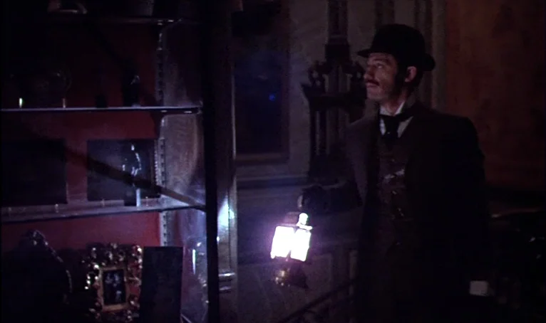 The Thief of Paris (1967) movie still: medium — A dimly lit room with glass display cases containing artifacts and ornate framed items. A man in a…