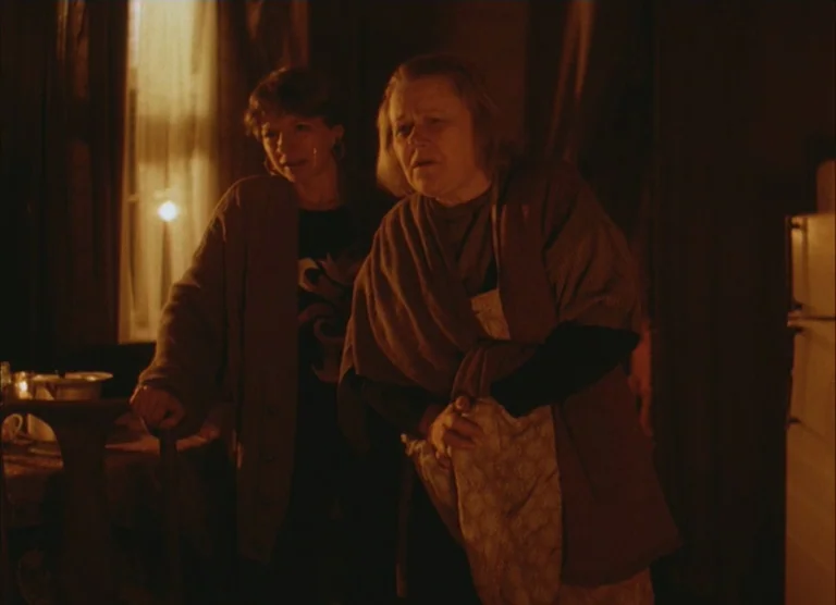 Russian Symphony (1994) movie still: medium — A dimly lit room at night features two women standing near a table. They look off-camera while…