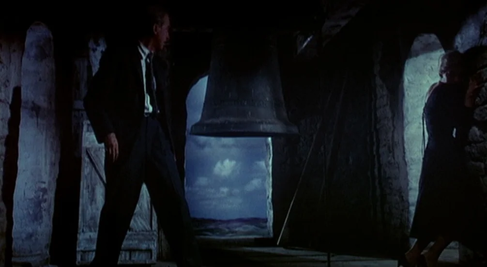 Vertigo (1958) movie still: fullbody — A dark stone bell tower interior features a large central hanging bell and stone pillars. A man in a suit…