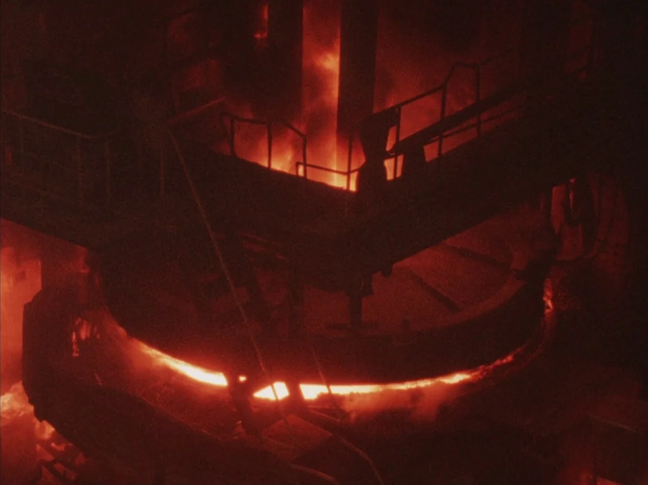 Tetsuo II: Body Hammer (1992) movie still: establishing — A dark industrial factory floor features heavy steel machinery and scaffolding over molten…