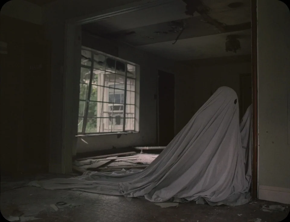 A Ghost Story (2017) movie still: medium — A dilapidated, empty room features peeling paint, debris on the floor, and dark corners. A figure draped…