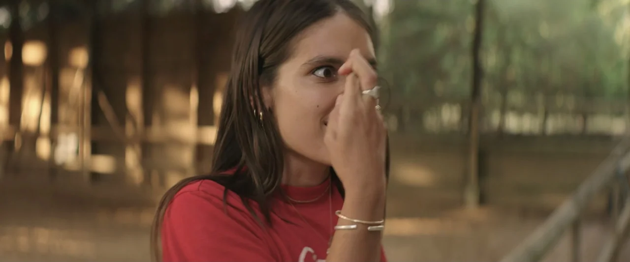 The Only One (2021) movie still: closeup — An outdoor corral with wooden fence posts in a golden sunset environment. A young woman in a red shirt…