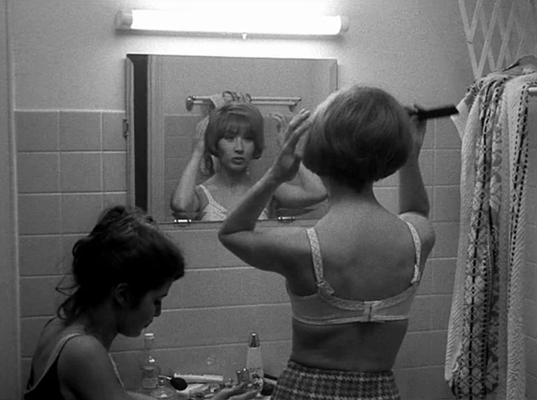 Masculin Féminin (1966) movie still: medium — A small tiled bathroom features a large wall mirror and a mounted light fixture. One woman brushes her…