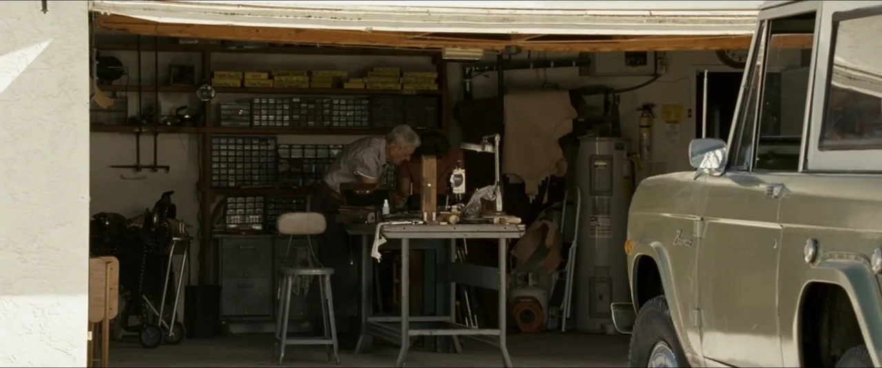 Into the Wild (2007) movie still: medium — A cluttered residential garage filled with storage shelves, tools, and a water heater unit. Two men work…