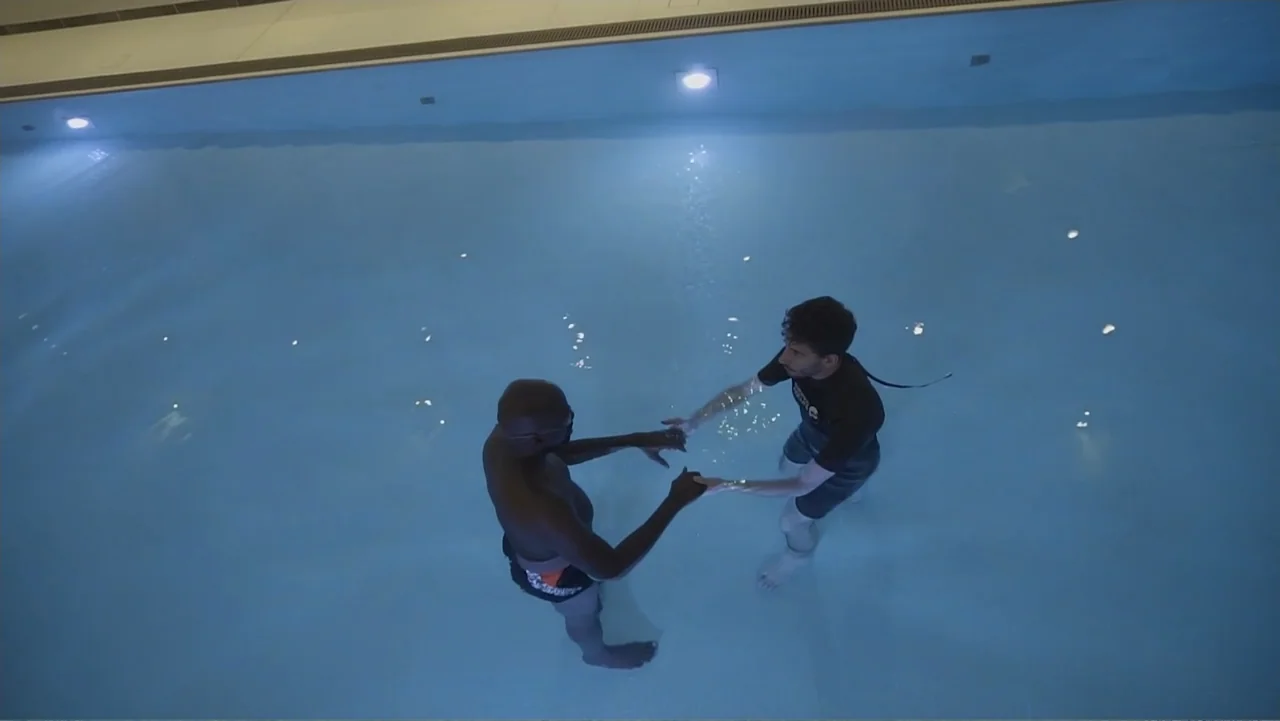 A Film Called Blacks Can't Swim (My Journey My Story) (2020) movie still: wide — A brightly lit indoor swimming pool with white tile and clear blue…