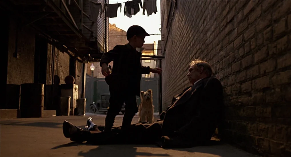 Miller’s Crossing (1990) movie still: fullbody — A narrow alley with brick walls and laundry hanging on a line overhead. A young boy stands next to…