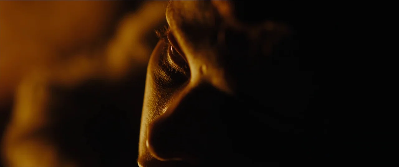 Out of Darkness (2022) movie still: closeup — A dark, underexposed environment leaves most of the frame in deep shadow. Only the side of a human…