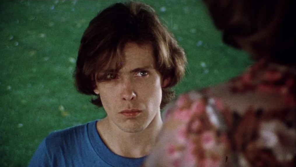 Martin (1977) movie still: closeup — A young man stands outdoors against a bright green grassy background in daylight. He looks toward an unseen…
