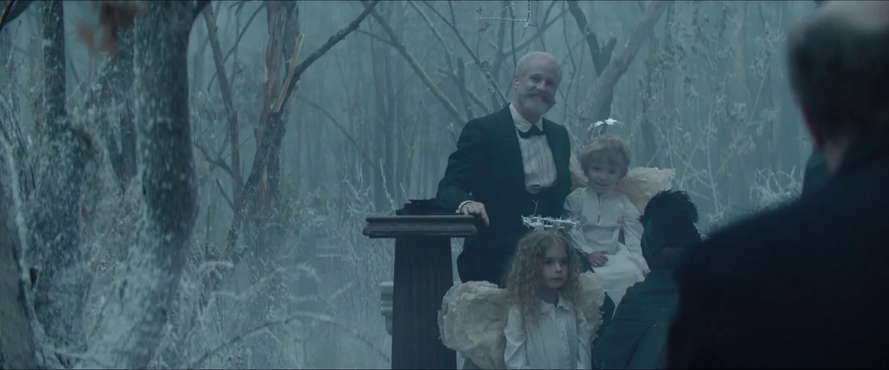 Tchaikovsky’s Wife (2022) movie still: medium — A man in a suit poses with two young children dressed as angels outdoors. The setting is a dense…