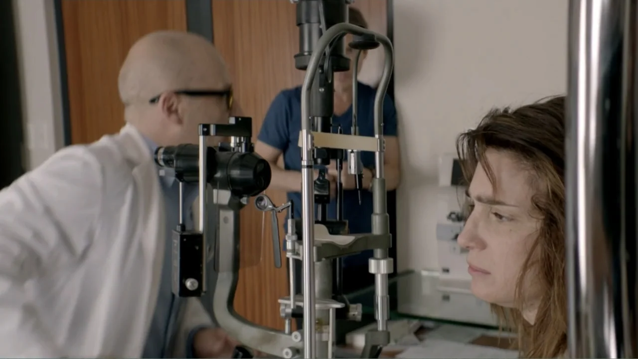 I Married a Dumbass (2016) movie still: medium — A clinical office features an ophthalmic slit lamp machine positioned on a desk. An eye doctor…