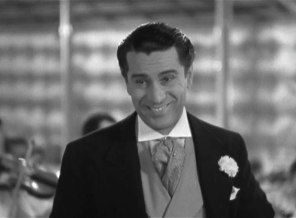 Swing Time (1936) movie still: medium — A formal ballroom setting features blurred figures of musicians in the background. A man dressed in evening…