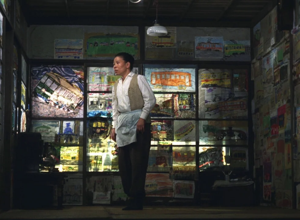 Dodes’ka-den (1970) movie still: fullbody — A room with walls completely covered in numerous colorful hand-drawn pictures of trains. A man stands in…